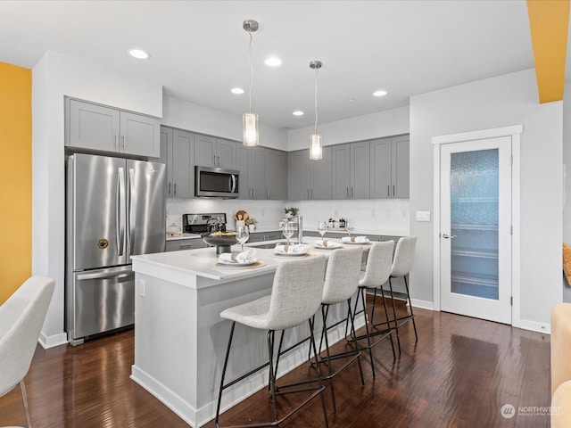 kitchen featuring dark wood-type flooring, a breakfast bar area, an island with sink, gray cabinetry, and appliances with stainless steel finishes