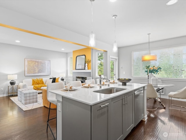 kitchen featuring light stone counters, pendant lighting, sink, gray cabinetry, and a center island with sink