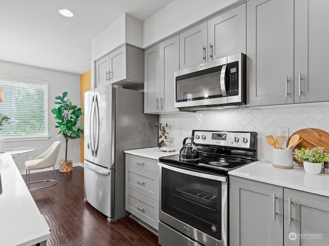 kitchen featuring light stone counters, dark hardwood / wood-style floors, gray cabinetry, stainless steel appliances, and backsplash