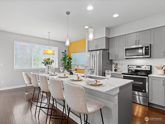 kitchen featuring light stone countertops, stainless steel appliances, decorative light fixtures, a kitchen island with sink, and dark hardwood / wood-style floors