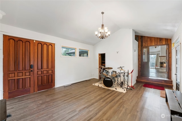 entryway featuring a notable chandelier, hardwood / wood-style flooring, wood walls, and vaulted ceiling