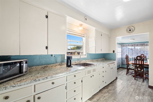 kitchen with white cabinetry, sink, light stone counters, and light wood-type flooring