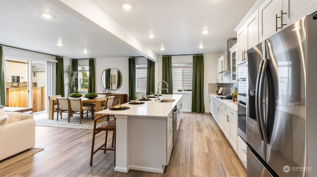 kitchen featuring a breakfast bar, sink, stainless steel fridge, a kitchen island with sink, and white cabinets