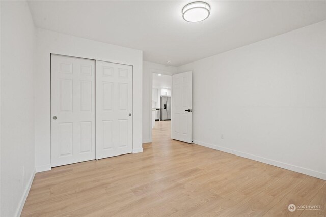 unfurnished bedroom with light hardwood / wood-style floors, a closet, and stainless steel refrigerator with ice dispenser