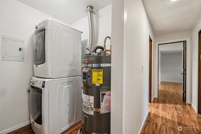 laundry area featuring stacked washer and dryer, electric panel, secured water heater, and hardwood / wood-style flooring