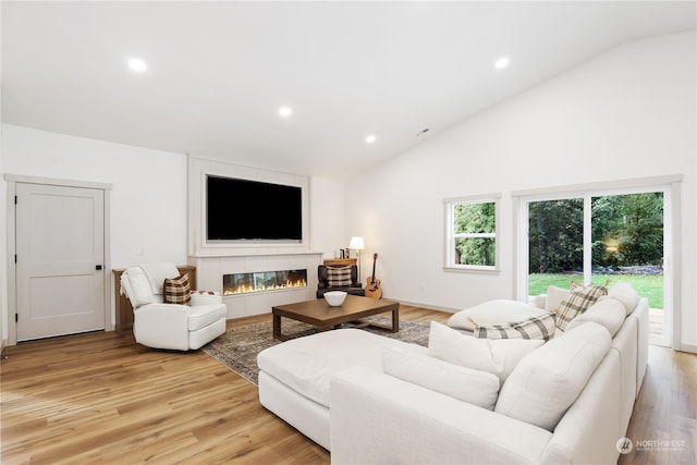 living room featuring high vaulted ceiling, light wood-type flooring, and a tile fireplace