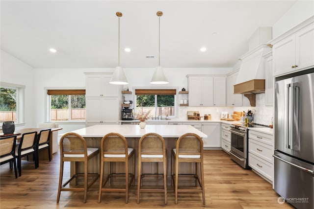 kitchen with appliances with stainless steel finishes, hanging light fixtures, white cabinets, a center island, and light hardwood / wood-style flooring