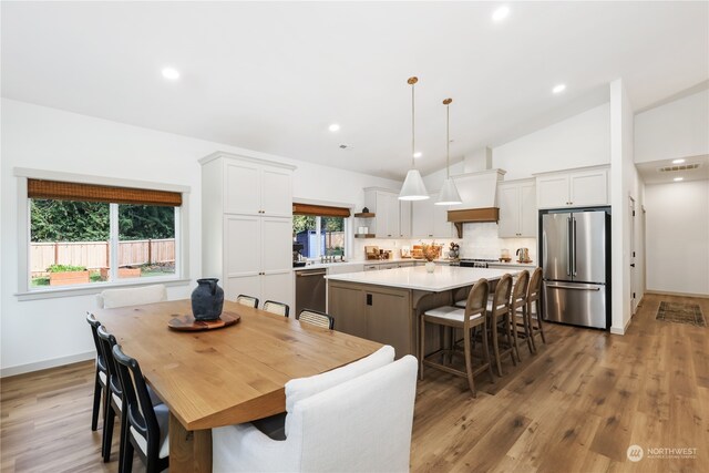 dining room with light wood-type flooring, a healthy amount of sunlight, and lofted ceiling