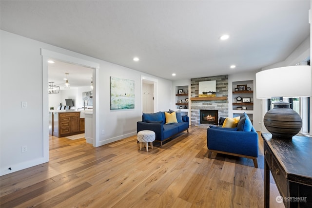 living room with light hardwood / wood-style flooring, built in features, and a stone fireplace