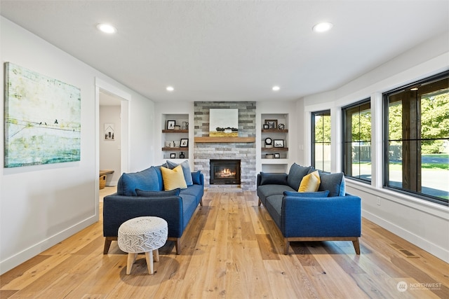 living room with built in shelves, light hardwood / wood-style floors, and a fireplace