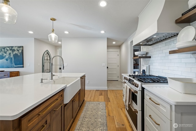 kitchen featuring pendant lighting, light hardwood / wood-style floors, high end stove, white cabinets, and wall chimney range hood