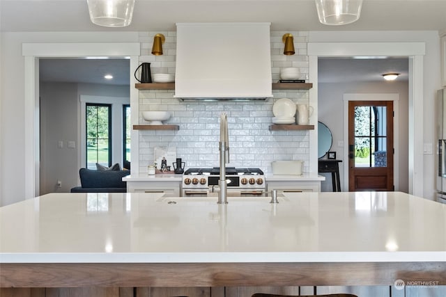 kitchen with a wealth of natural light, backsplash, stainless steel stove, and decorative light fixtures