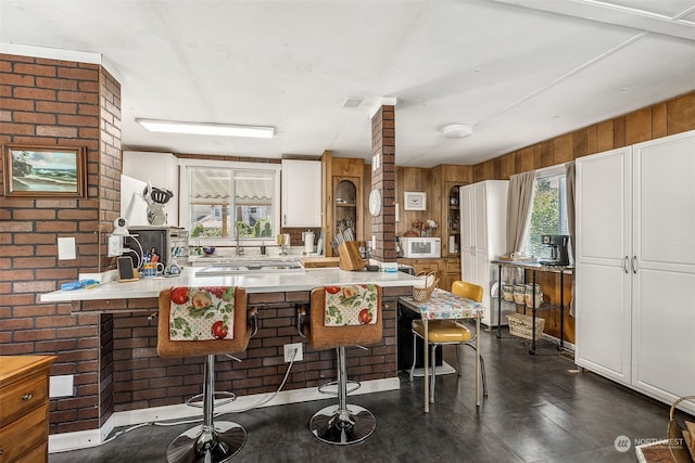 kitchen featuring a wealth of natural light, white cabinets, a kitchen bar, and wooden walls