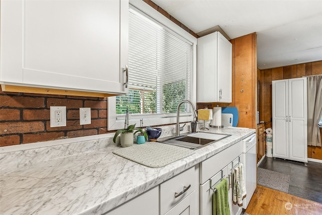 kitchen with wood walls, white cabinetry, and sink