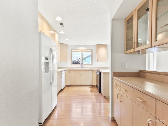 kitchen featuring light hardwood / wood-style floors, white appliances, light brown cabinetry, sink, and a textured ceiling