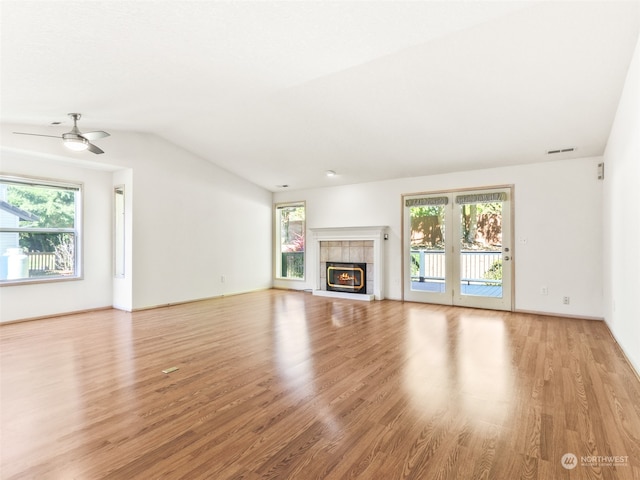 unfurnished living room with ceiling fan, lofted ceiling, a tiled fireplace, and light hardwood / wood-style floors