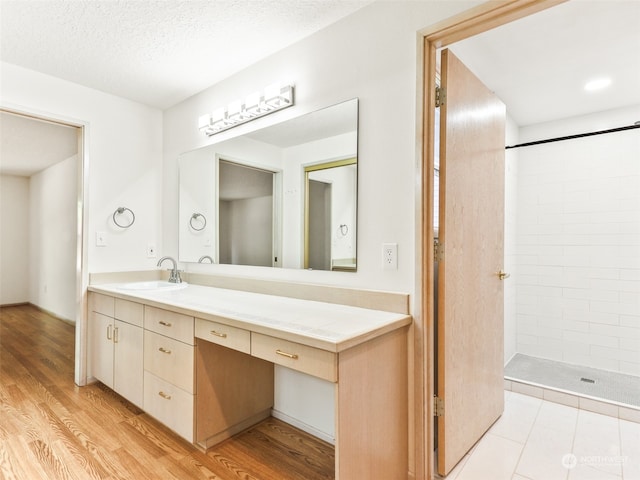 bathroom featuring vanity, hardwood / wood-style floors, a textured ceiling, and tiled shower