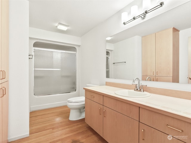 full bathroom featuring wood-type flooring, shower / bath combination with glass door, vanity, and toilet