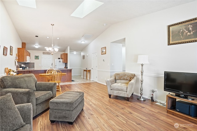 living room featuring vaulted ceiling with skylight, light hardwood / wood-style flooring, and a notable chandelier