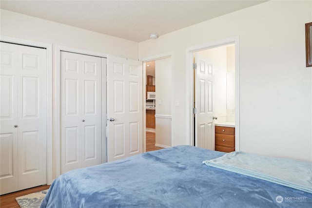 bedroom featuring hardwood / wood-style floors, ensuite bathroom, and multiple closets