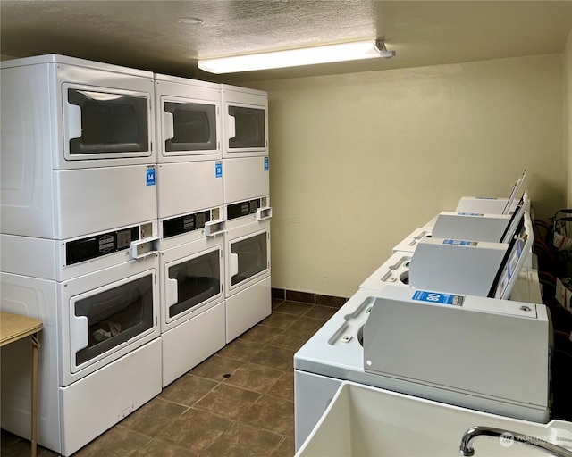 washroom with a textured ceiling, stacked washer / dryer, dark tile patterned floors, and separate washer and dryer