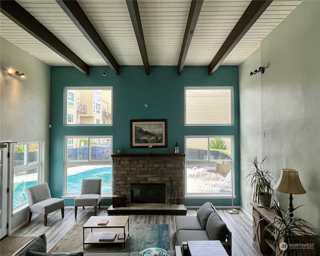 living room featuring beamed ceiling, light hardwood / wood-style flooring, a fireplace, and a healthy amount of sunlight