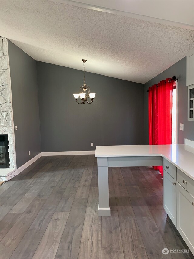 unfurnished dining area featuring dark hardwood / wood-style flooring, a chandelier, a textured ceiling, lofted ceiling, and a stone fireplace