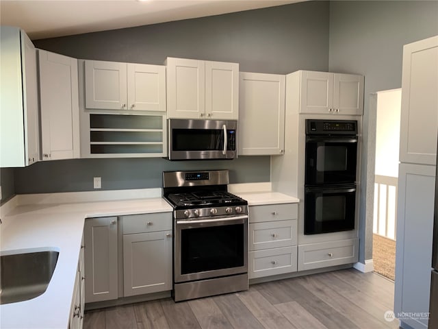 kitchen featuring sink, vaulted ceiling, white cabinetry, stainless steel appliances, and light hardwood / wood-style floors