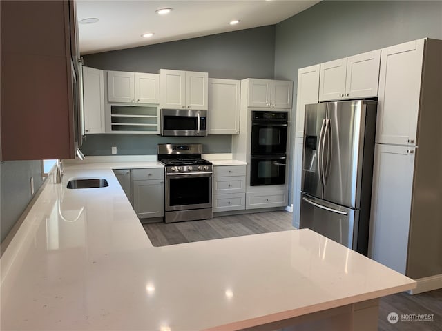 kitchen featuring sink, white cabinets, vaulted ceiling, stainless steel appliances, and hardwood / wood-style floors