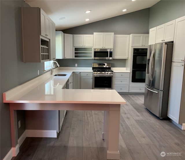 kitchen featuring white cabinetry, stainless steel appliances, a kitchen bar, lofted ceiling, and light hardwood / wood-style flooring