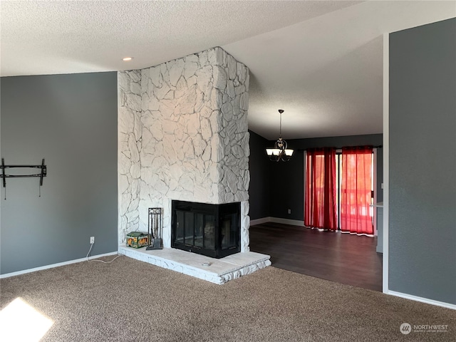 unfurnished living room featuring a stone fireplace, an inviting chandelier, dark wood-type flooring, and a textured ceiling