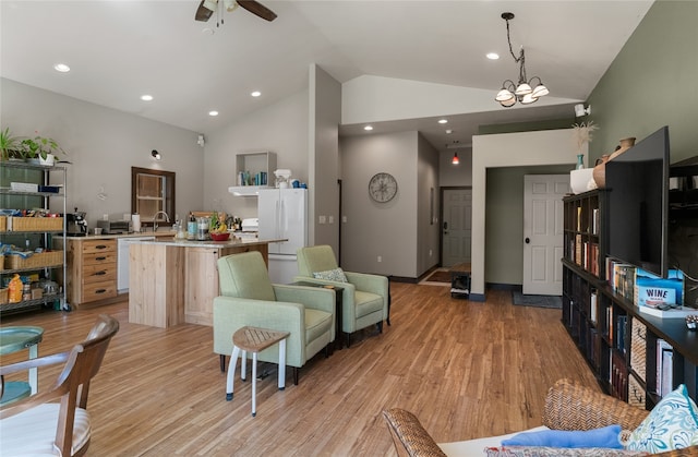 living room with light wood-type flooring, ceiling fan with notable chandelier, sink, and high vaulted ceiling