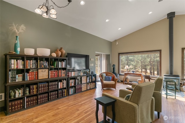 sitting room with an inviting chandelier, light wood-type flooring, a wood stove, and high vaulted ceiling