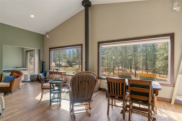 dining space with light hardwood / wood-style floors, high vaulted ceiling, and a wood stove