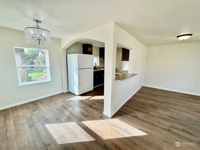 kitchen with white refrigerator, hanging light fixtures, sink, a chandelier, and hardwood / wood-style flooring