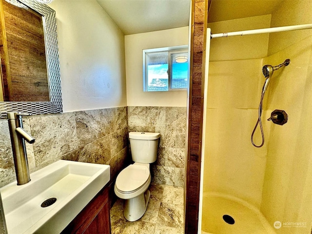 bathroom featuring toilet, tile walls, a wainscoted wall, vanity, and a stall shower