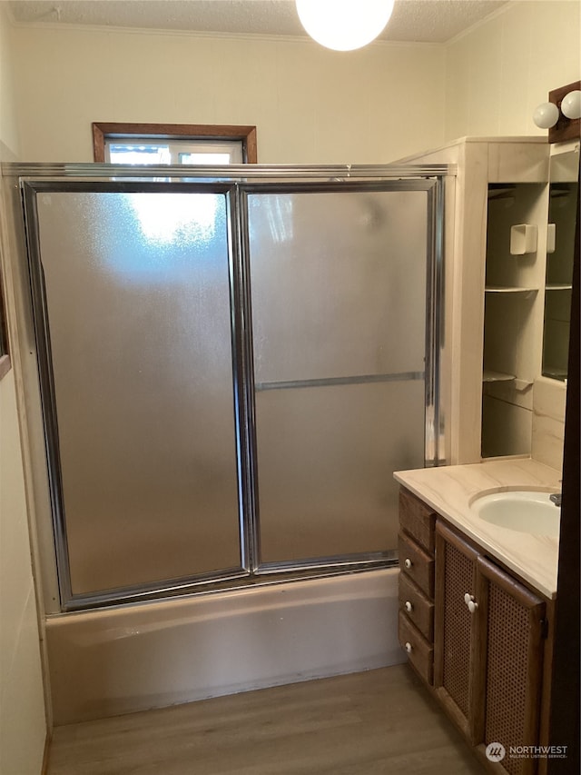 bathroom featuring wood-type flooring, vanity, combined bath / shower with glass door, and a textured ceiling