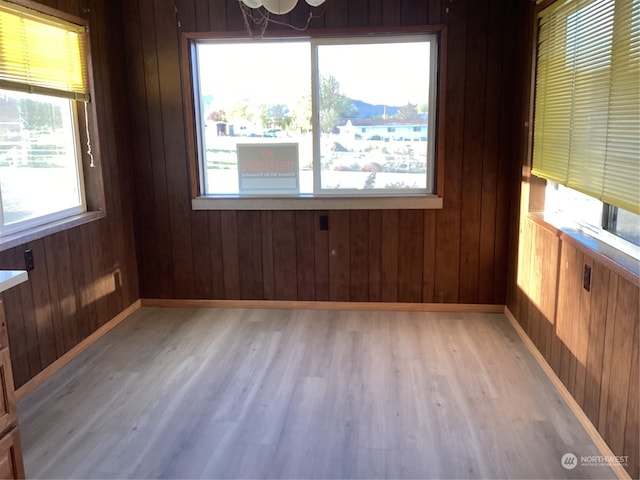 spare room with light hardwood / wood-style floors, a chandelier, and wooden walls