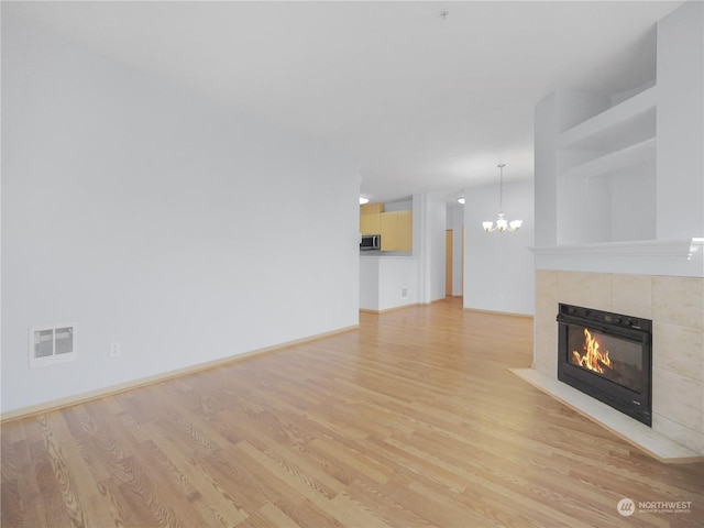 unfurnished living room featuring a tiled fireplace, an inviting chandelier, and light hardwood / wood-style flooring