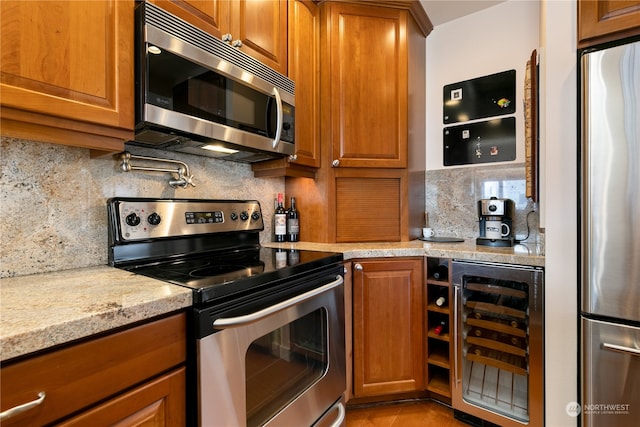 kitchen featuring beverage cooler, backsplash, appliances with stainless steel finishes, and light stone counters