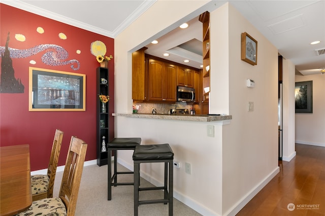 kitchen with kitchen peninsula, light hardwood / wood-style flooring, backsplash, crown molding, and a kitchen bar