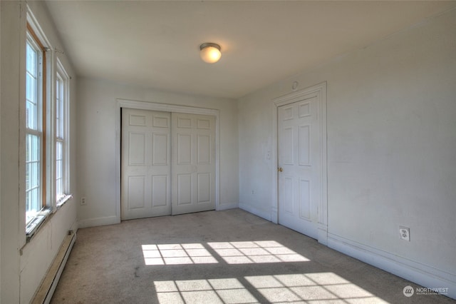 unfurnished bedroom with a baseboard heating unit, a closet, and light colored carpet