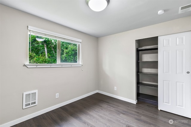 unfurnished bedroom with heating unit, a closet, and dark wood-type flooring