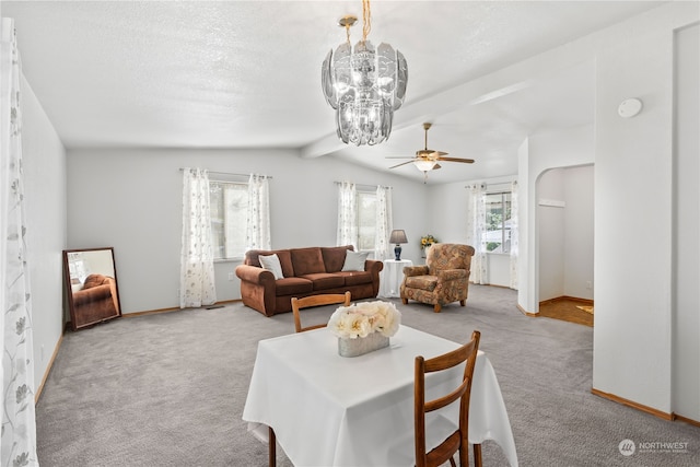 carpeted living room featuring a textured ceiling, ceiling fan with notable chandelier, lofted ceiling with beams, and plenty of natural light