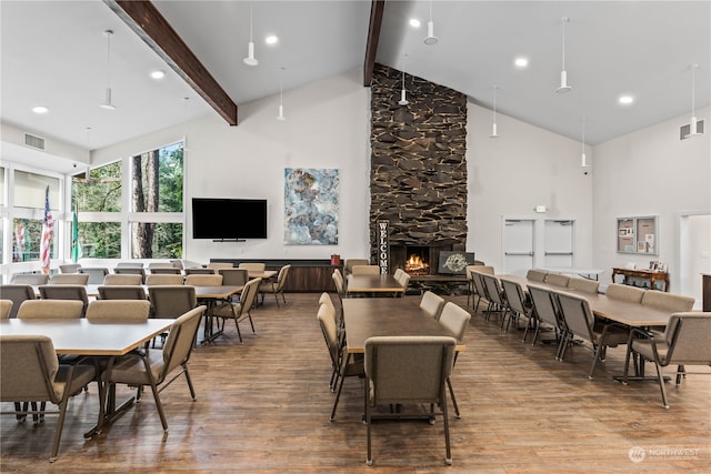 dining room featuring wood-type flooring, a stone fireplace, beam ceiling, and high vaulted ceiling