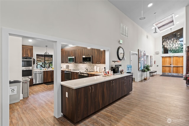 kitchen with appliances with stainless steel finishes, hanging light fixtures, tasteful backsplash, and light hardwood / wood-style flooring