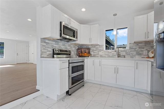 kitchen featuring pendant lighting, sink, white cabinets, stainless steel appliances, and backsplash