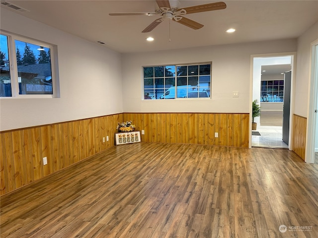 unfurnished room featuring wood-type flooring, wood walls, and ceiling fan