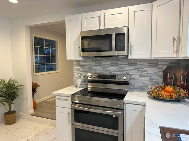 kitchen with stainless steel appliances, white cabinetry, light stone counters, and backsplash