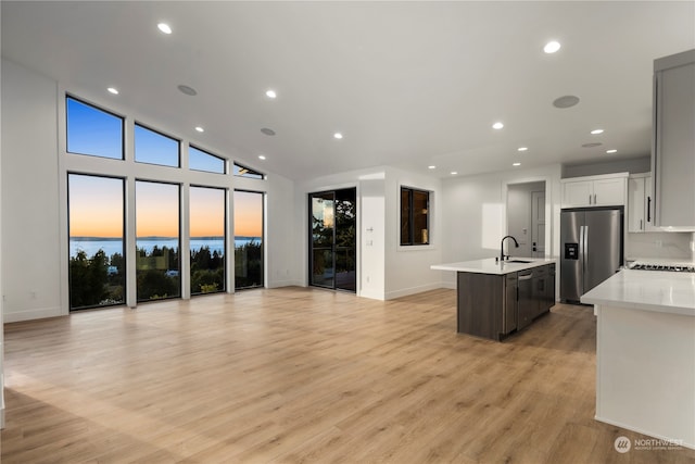 kitchen with white cabinets, a center island with sink, sink, light wood-type flooring, and appliances with stainless steel finishes